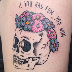 A tattoo of a skull topped with flowers, there is text above that curves with the top of the skull. The text reads "If you had fun, you won"